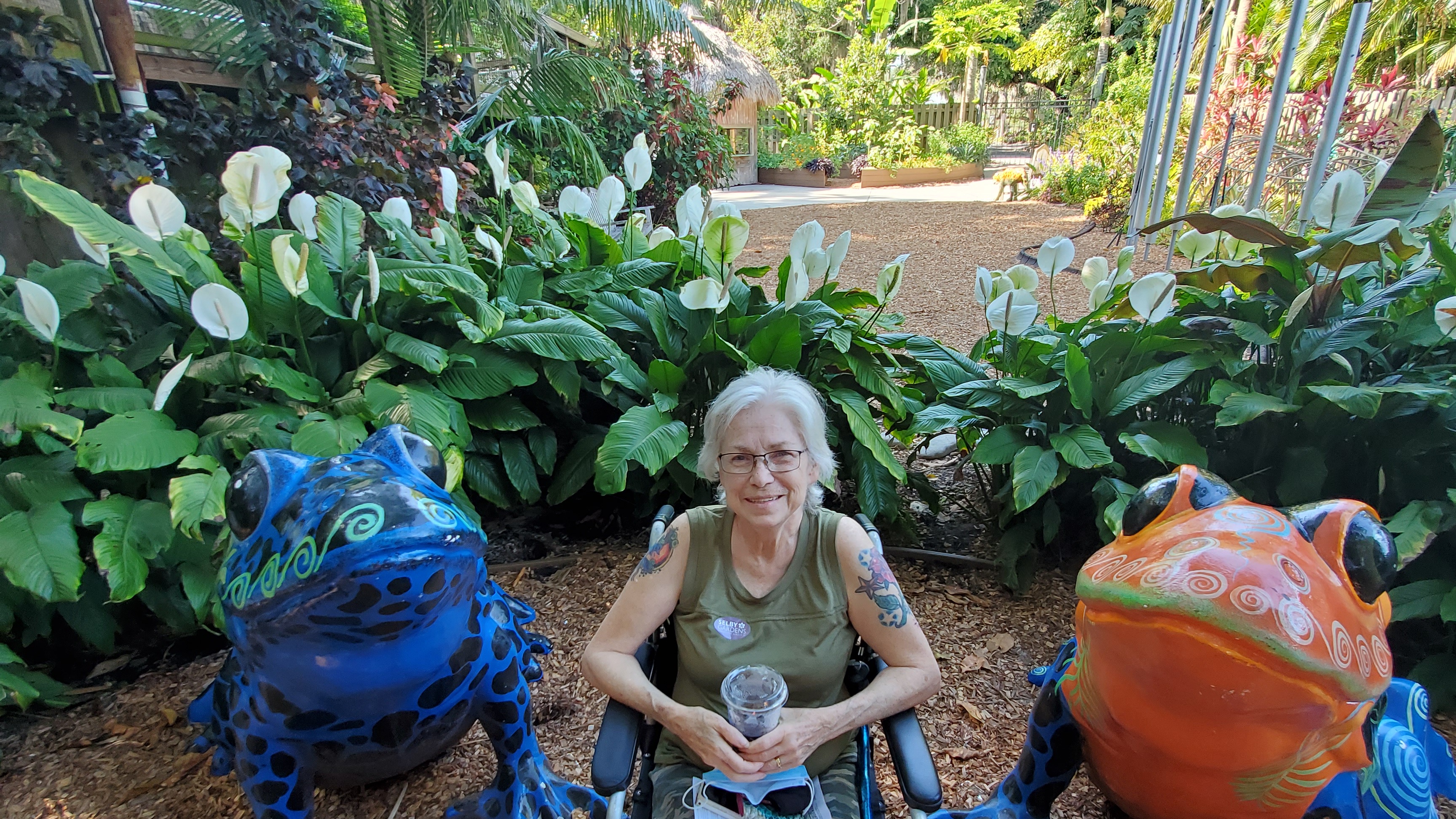 Shelva, my mom, sitting between two frog statues in front of a background of peace lillys.